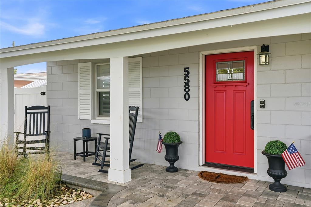 A front porch features a red door, two rocking chairs, and two potted plants — 5580 TANGELO ROAD, SEMINOLE, FL