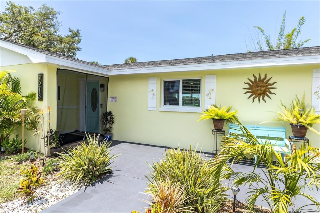 A light yellow house exterior features a front patio, a turquoise door, and potted plants — 7213 PENINSULAR DRIVE, NEW PORT RICHEY, FL
