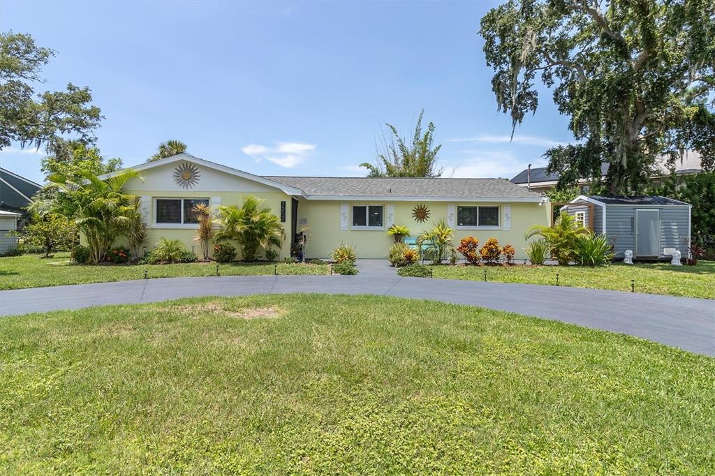 A single-story yellow house with a curved driveway and a detached shed in the yard — 7213 PENINSULAR DRIVE, NEW PORT RICHEY, FL