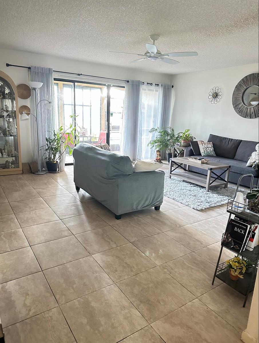 A living room features tile flooring, a gray sofa, a coffee table, and sliding glass doors — 5807 Parkwalk Drive, Boynton Beach FL 33472, BOYNTON BEACH, FL