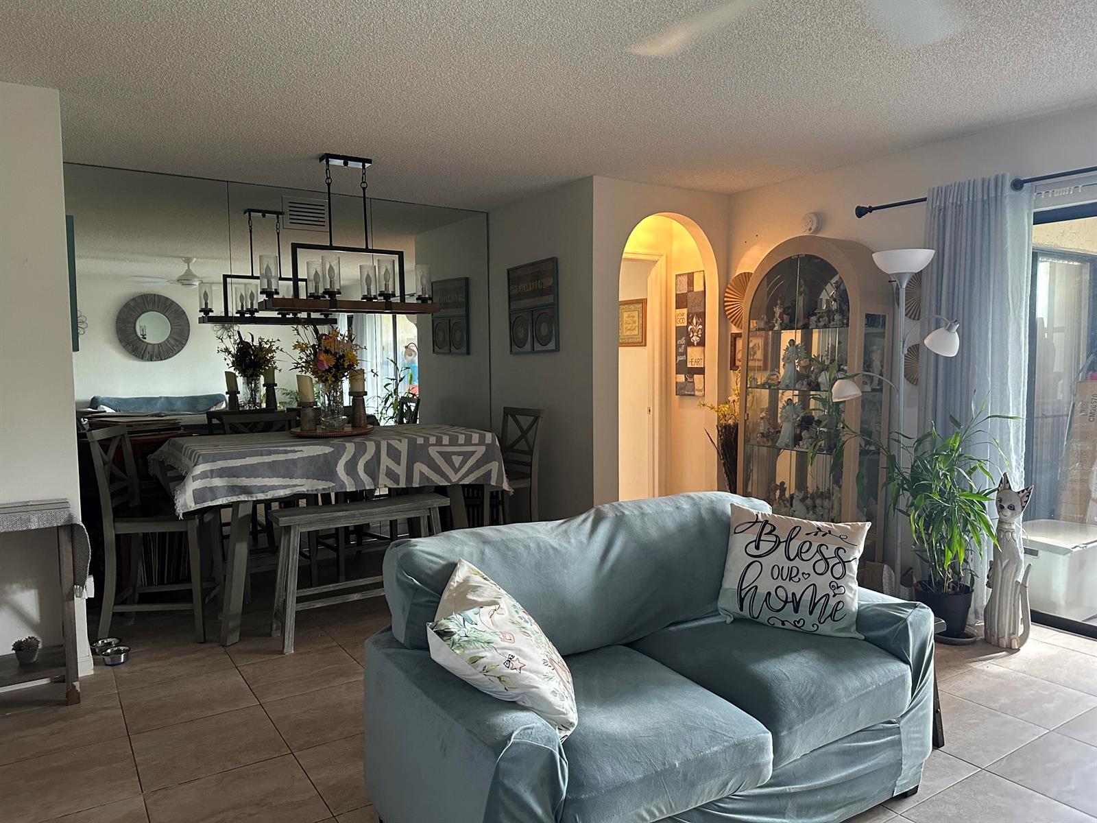 A living room with a blue loveseat, dining area, mirrored wall, and arched doorway — 5807 Parkwalk Drive, Boynton Beach FL 33472, BOYNTON BEACH, FL