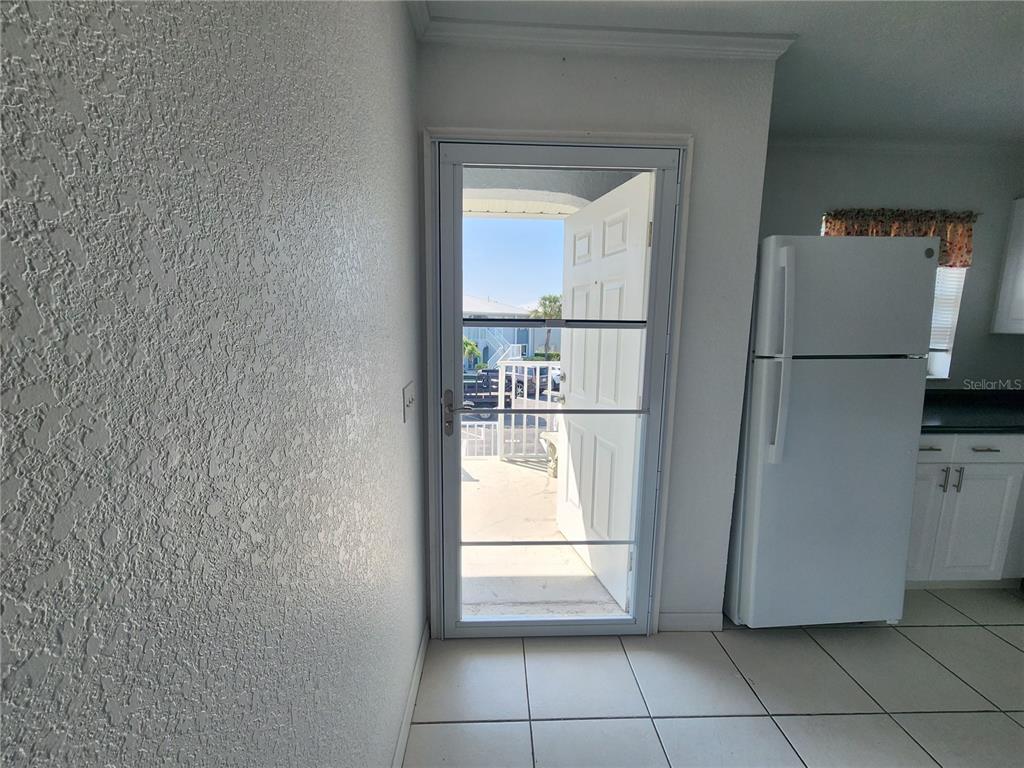 A white refrigerator stands next to an open door leading to an outdoor patio area — 25050 SANDHILL BOULEVARD UNIT B1, PUNTA GORDA, FL