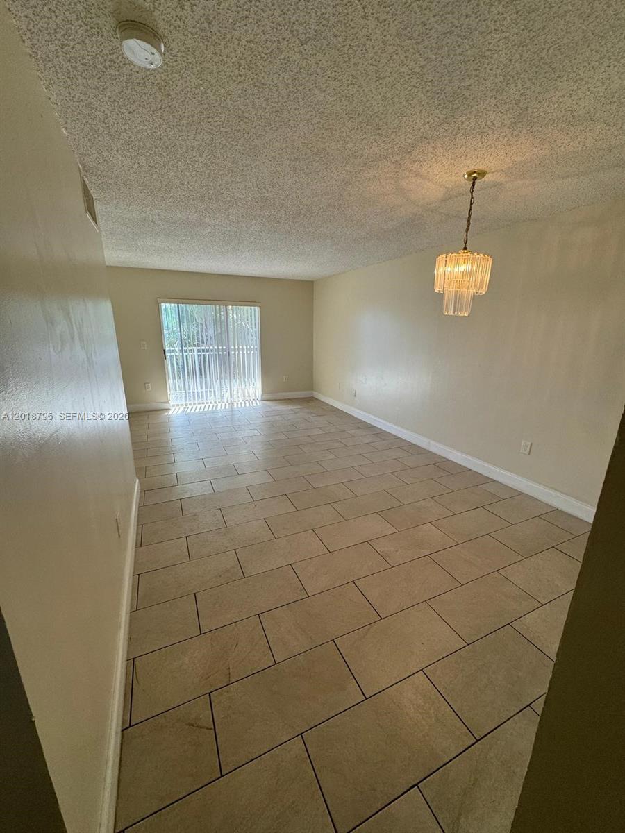 An empty room features beige tile flooring, a textured ceiling, and a hanging crystal chandelier — 11307 SW 200th St # B, Miami FL 33157, MIAMI, FL