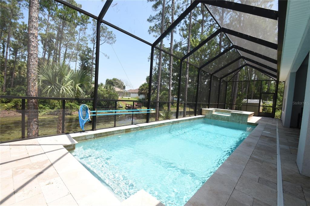 A screened-in swimming pool and spa overlook a wooded area and a small pond — 108 PLAIN VIEW DRIVE, PALM COAST, FL