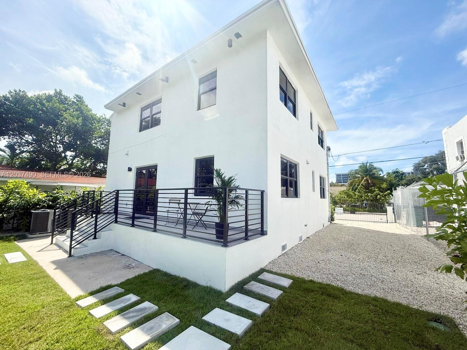 A white two-story house features a raised deck with black railings and a gravel yard — 243 NW 32nd St, Miami FL 33127, MIAMI, FL