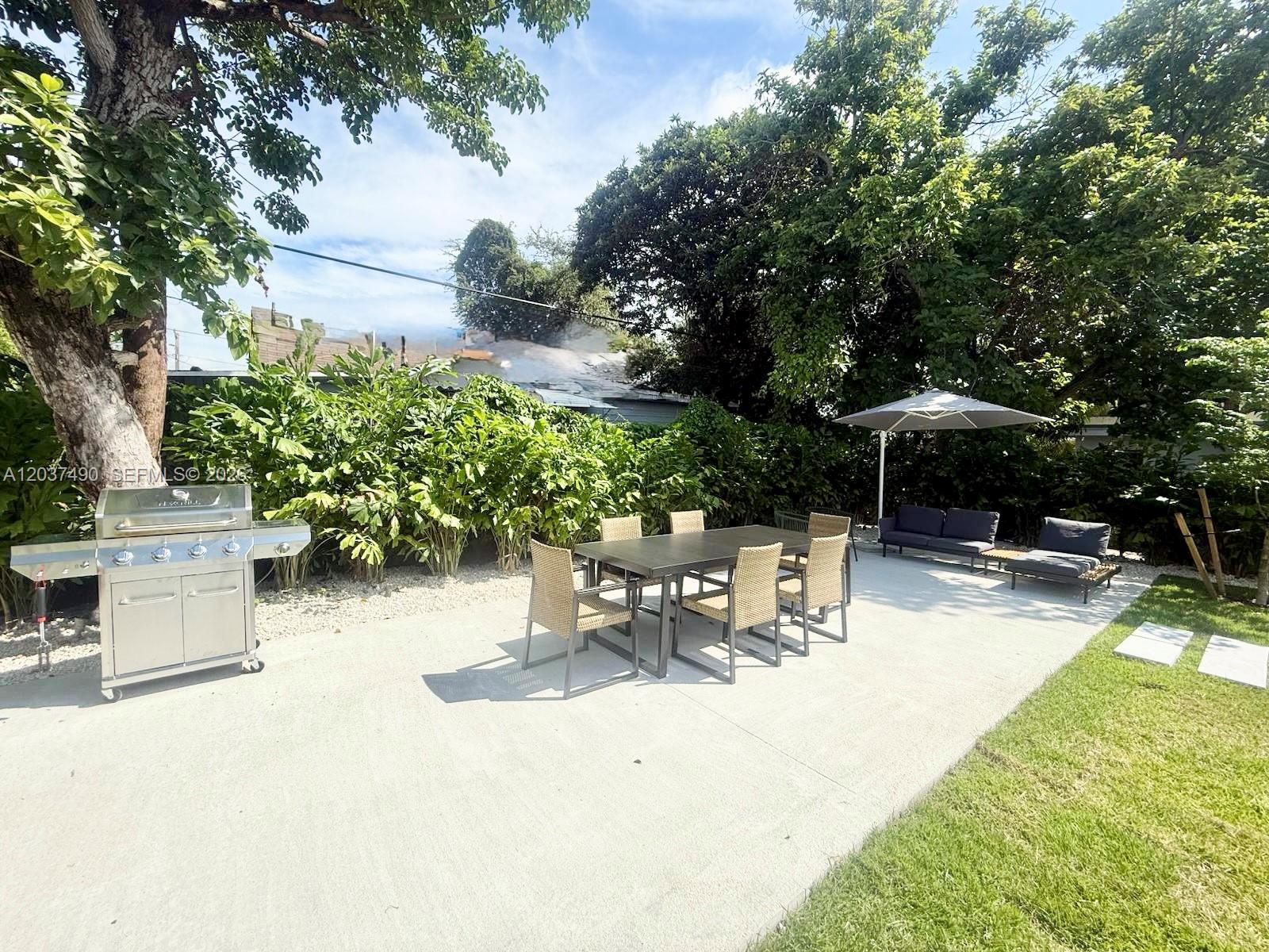 A backyard patio features a stainless steel grill, dining set, and lounge seating under trees — 243 NW 32nd St, Miami FL 33127, MIAMI, FL