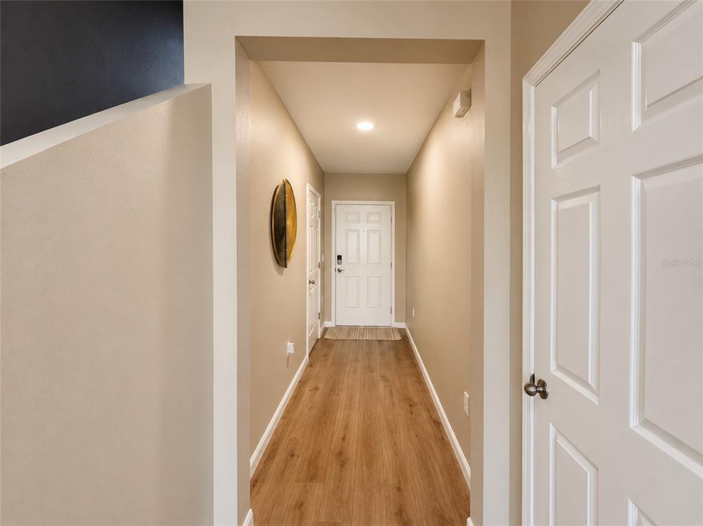 A hallway with wood-look flooring leads to a white front door — 1352 DERRY AVENUE, HAINES CITY, FL