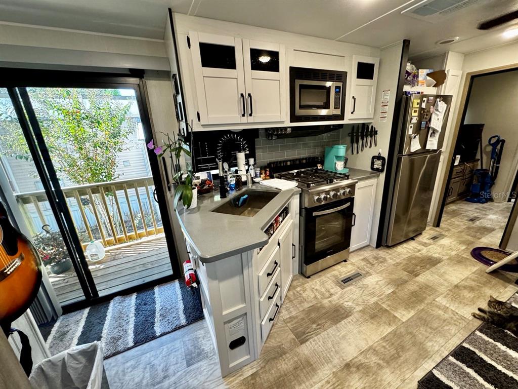 A kitchen in a recreational vehicle features white cabinets, stainless steel appliances, and a sliding door — 14423 NE 252ND COURT ROAD, SALT SPRINGS, FL