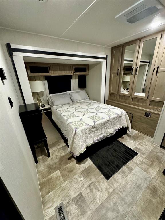 A bedroom in a recreational vehicle features a queen bed, wood-toned cabinetry, and wood-look flooring — 14423 NE 252ND COURT ROAD, SALT SPRINGS, FL
