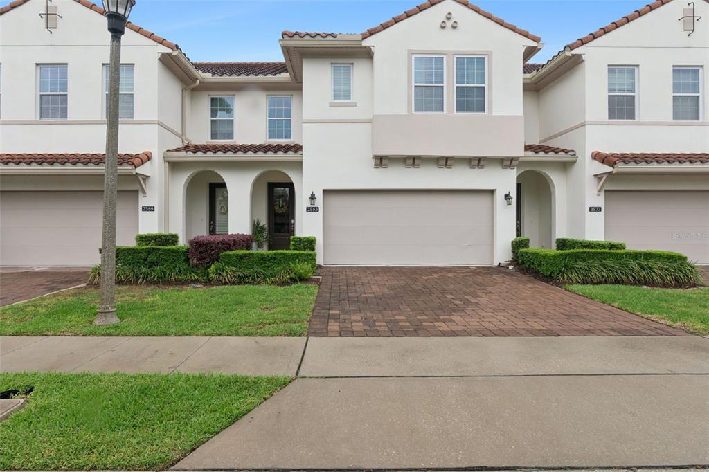 The exterior of a two-story townhouse features a paved driveway, a garage, and landscaping — 2583 CIRCOLO LANE, APOPKA, FL
