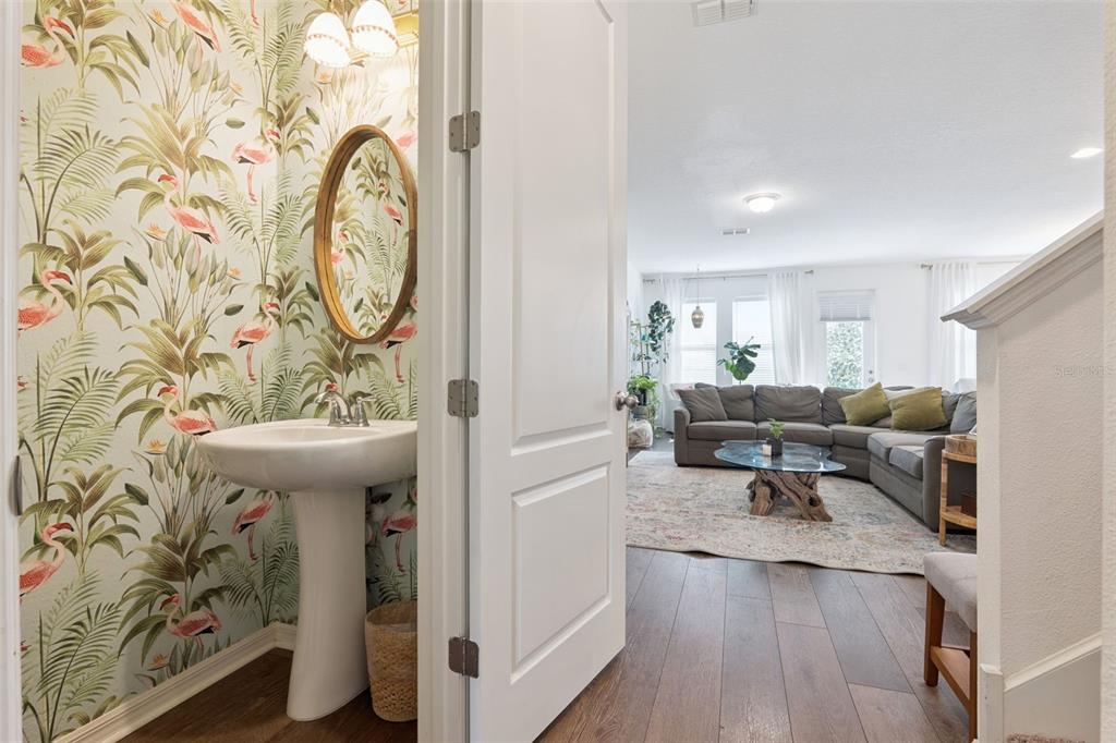 A view from a hallway into a powder room with flamingo wallpaper and a living room — 2583 CIRCOLO LANE, APOPKA, FL