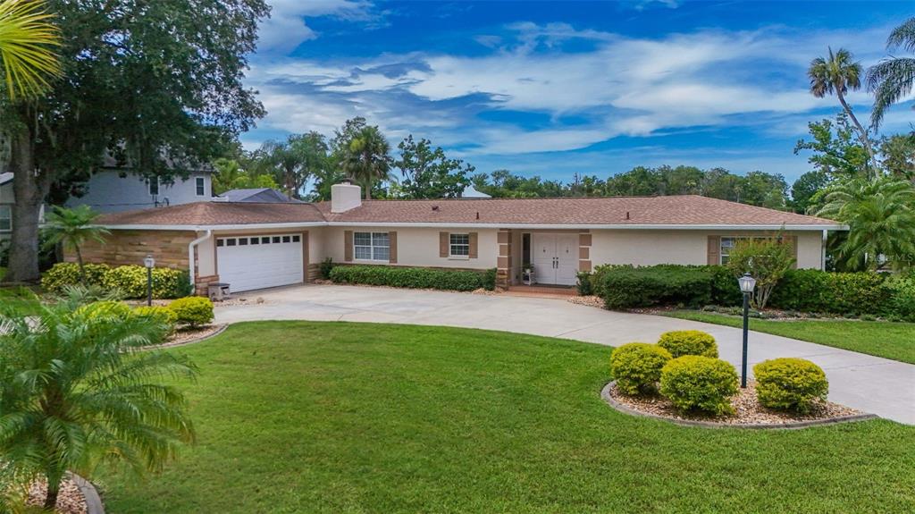 A single-story house with a white garage, beige exterior, and a large front lawn — 1202 SE KINGS BAY DRIVE, CRYSTAL RIVER, FL