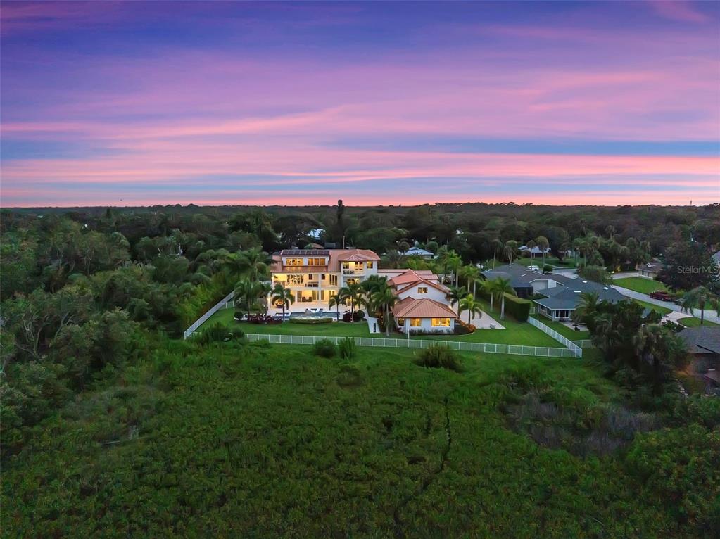 An aerial view shows a large multi-story house with a pool and fenced yard at sunset — 1511 S RIVERSIDE DRIVE, NEW SMYRNA BEACH, FL
