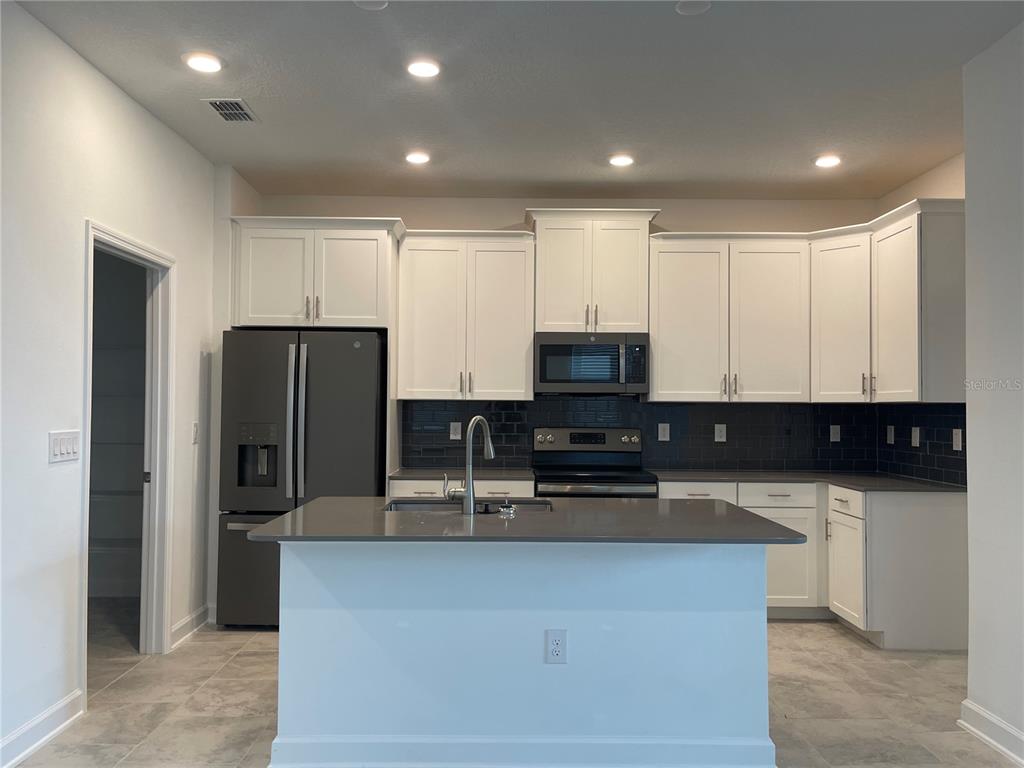 A kitchen features white cabinets, a gray island, dark countertops, and a dark tile backsplash — 9777 PETITION WAY, ORLANDO, FL