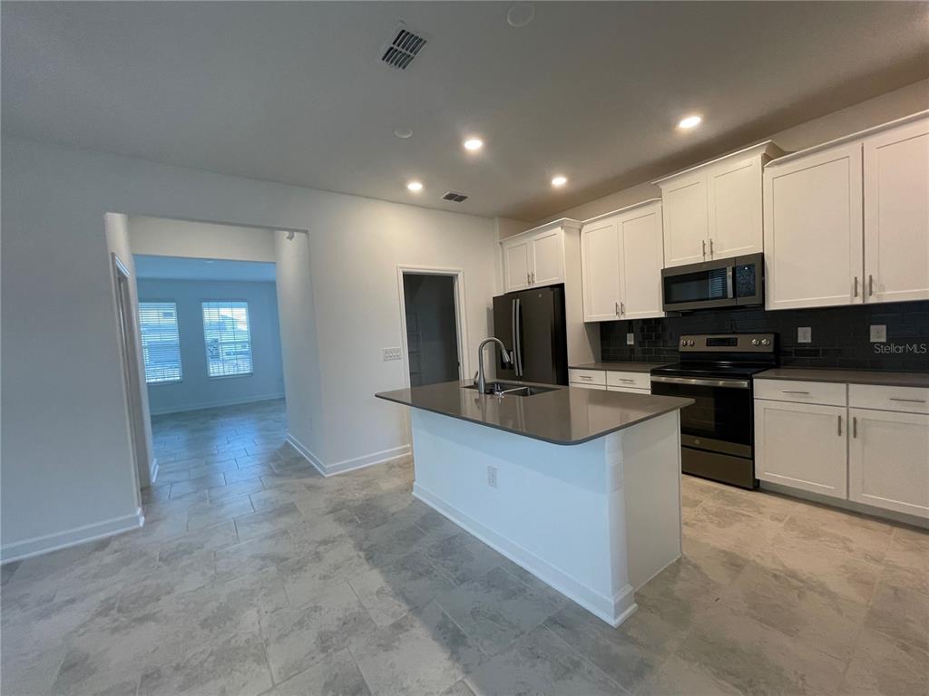 A kitchen features white cabinets, a gray island, stainless steel appliances, and tile flooring — 9777 PETITION WAY, ORLANDO, FL