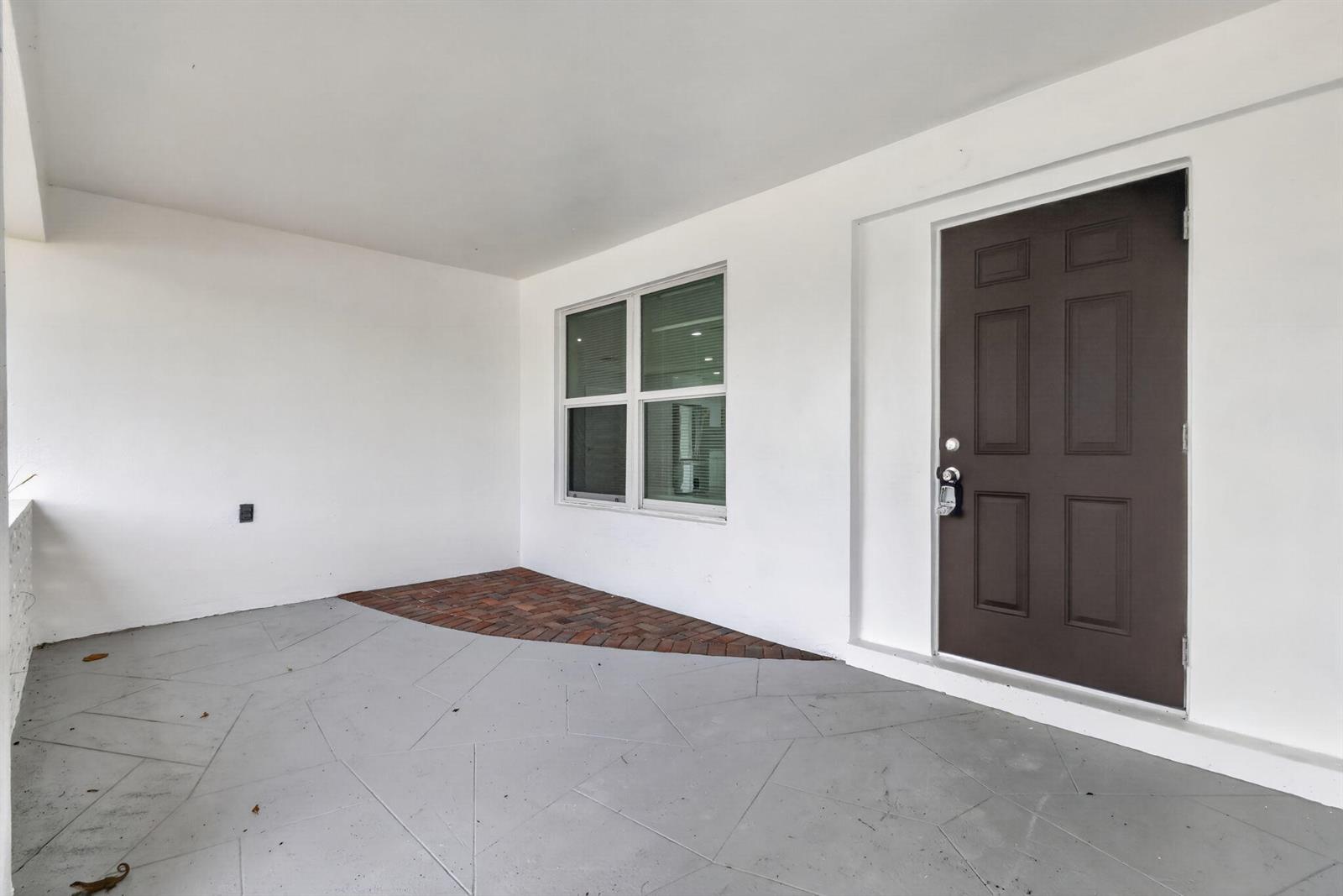A covered porch features a gray concrete floor, a brick accent area, and a brown door — 1408 Cochran Drive, FL 33461, FL