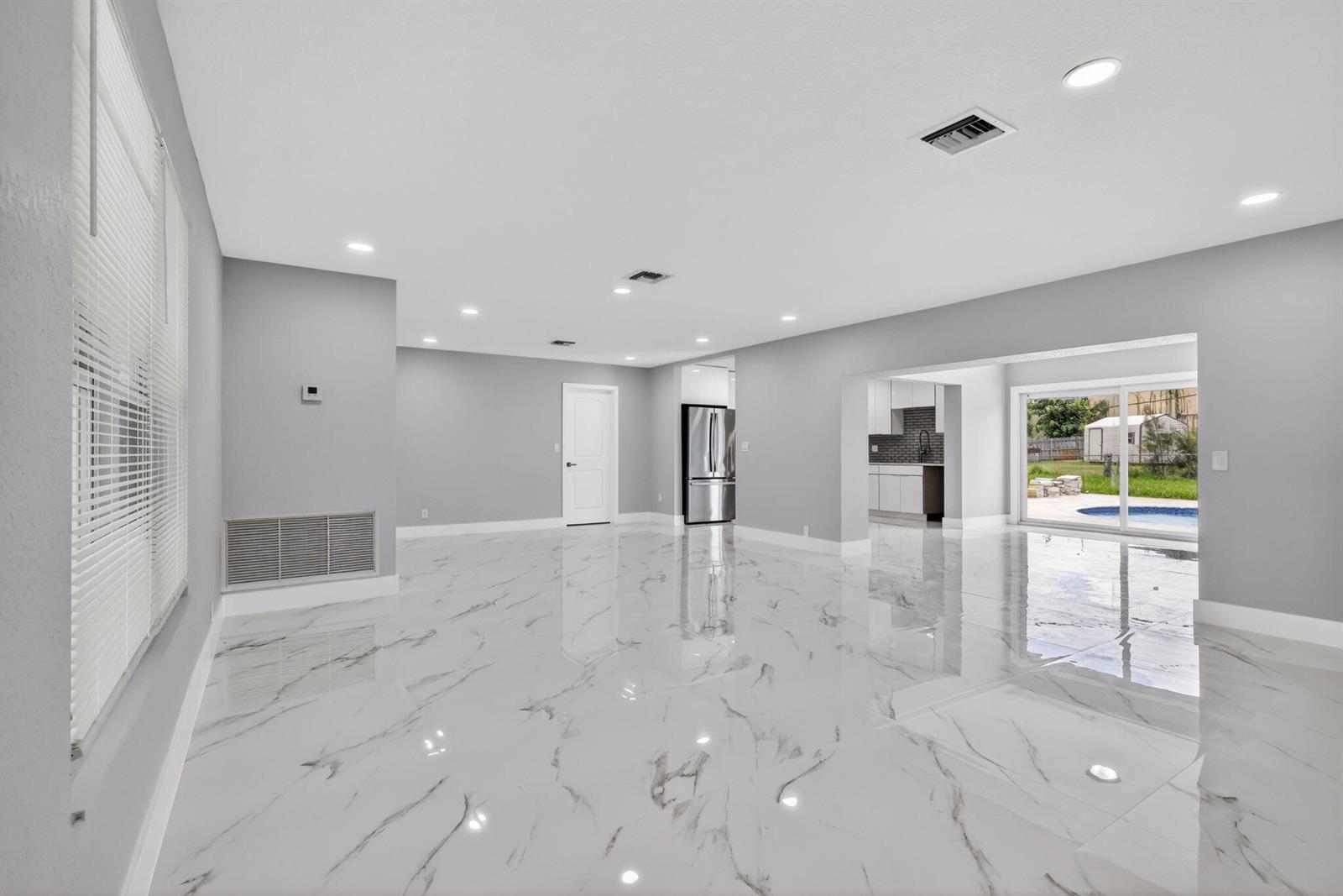 A spacious, open-concept living area features white marble-look tile flooring, recessed lighting, and a kitchen — 1408 Cochran Drive, FL 33461, FL