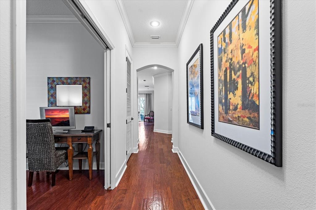 A hallway with hardwood floors leads to an arched doorway, featuring framed art and a desk — 5 OCEAN CREST WAY UNIT 1414, PALM COAST, FL