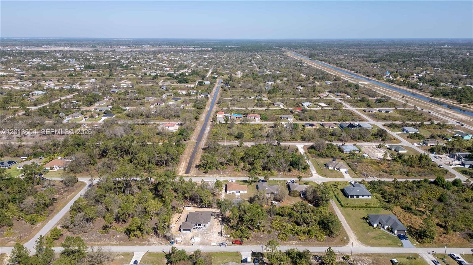 An aerial view shows a residential neighborhood with scattered houses, wooded lots, and a canal — 2522 W 53RD ST, Lehigh Acres FL 33971, LEHIGH ACRES, FL
