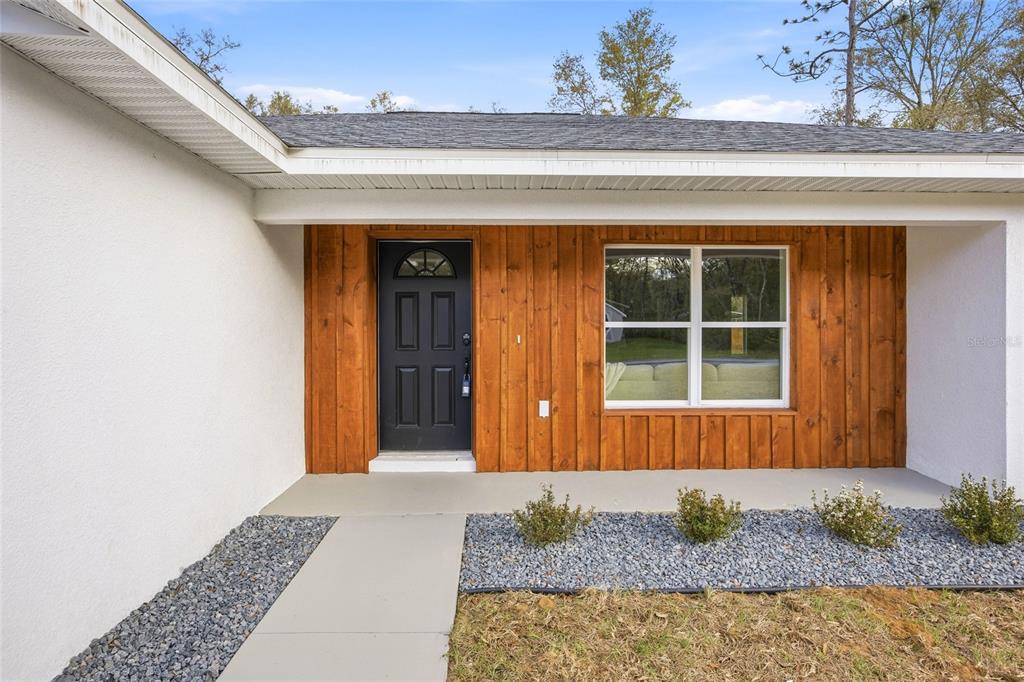A front porch with a black door and wood-paneled siding on a white house — 2116 W BEACH PLUM DRIVE, CITRUS SPRINGS, FL