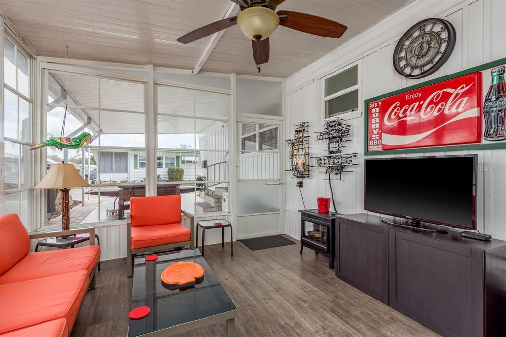 A sunroom features orange seating, a television, a ceiling fan, and large windows looking outside — 2331 BELLEAIR ROAD UNIT 906, CLEARWATER, FL