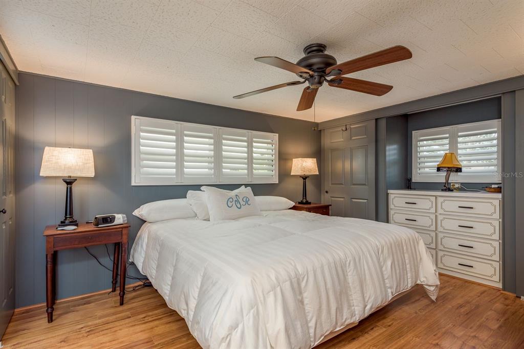 A bedroom with gray walls, wood-look flooring, a ceiling fan, and a white-covered bed — 2331 BELLEAIR ROAD UNIT 906, CLEARWATER, FL