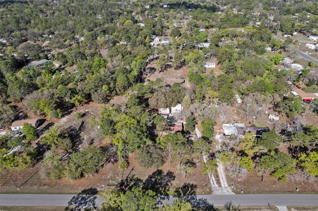 An aerial view shows a wooded residential lot with several buildings and a paved road — 6850 S MAXWELL POINT, HOMOSASSA, FL