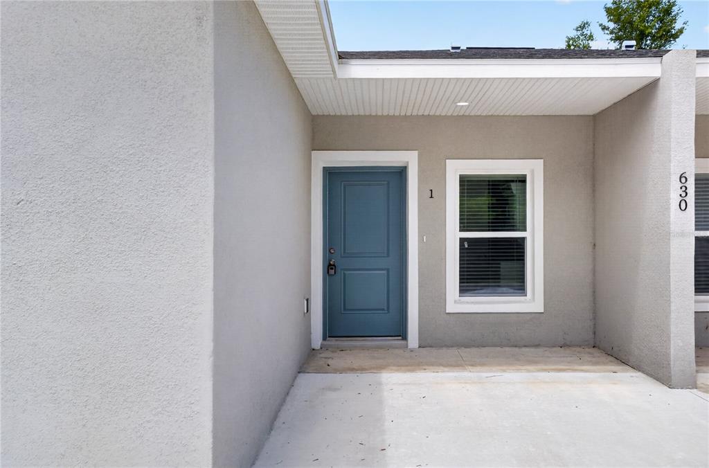 A blue front door and a window are set into the gray stucco exterior wall — 630 NW 59TH AVENUE UNIT 1, OCALA, FL