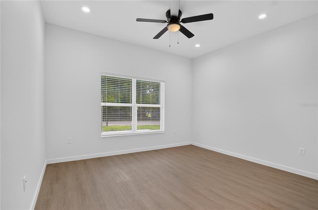 A bright, empty room features light wood-look flooring, white walls, and a ceiling fan — 630 NW 59TH AVENUE UNIT 1, OCALA, FL