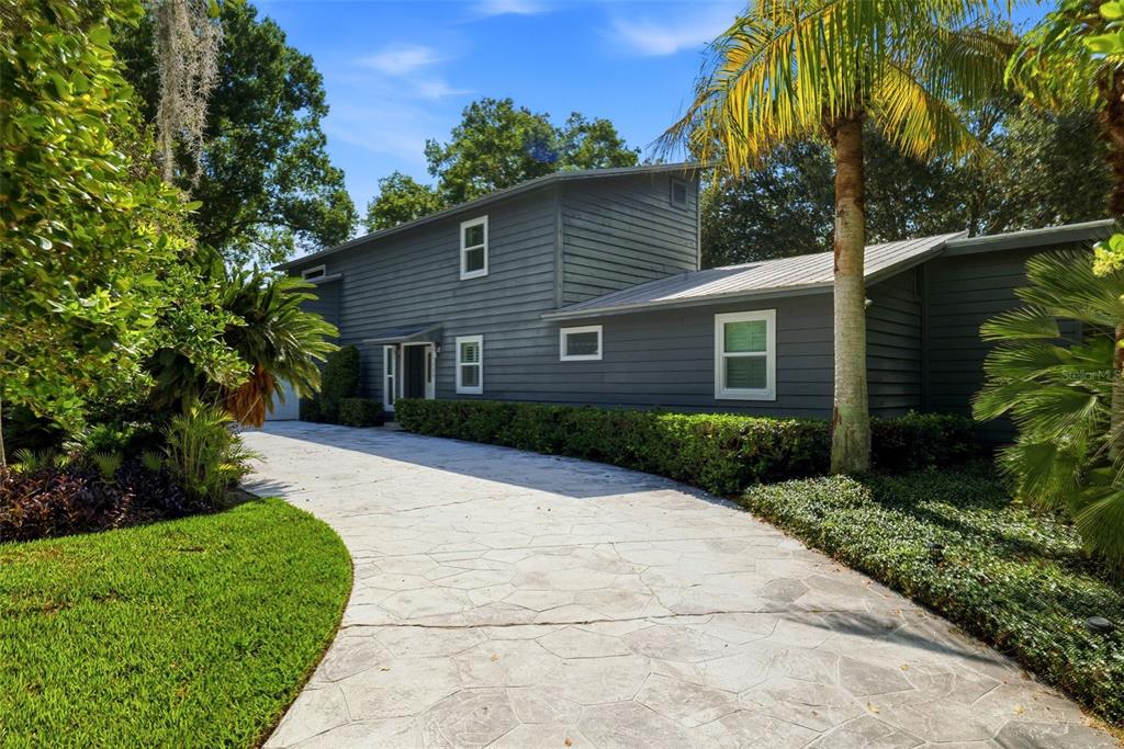 A gray two-story house with horizontal siding features a stone-patterned driveway and lush landscaping — 708 WARREN ROAD, LUTZ, FL