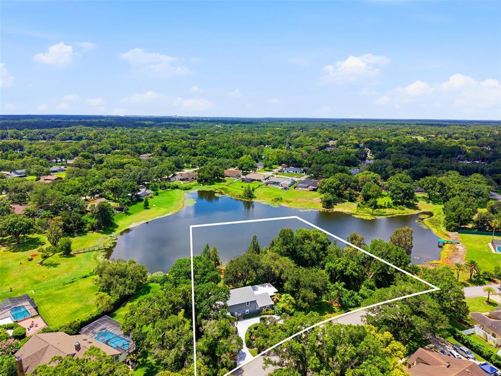 An aerial view shows a house on a wooded lot bordering a lake — 708 WARREN ROAD, LUTZ, FL