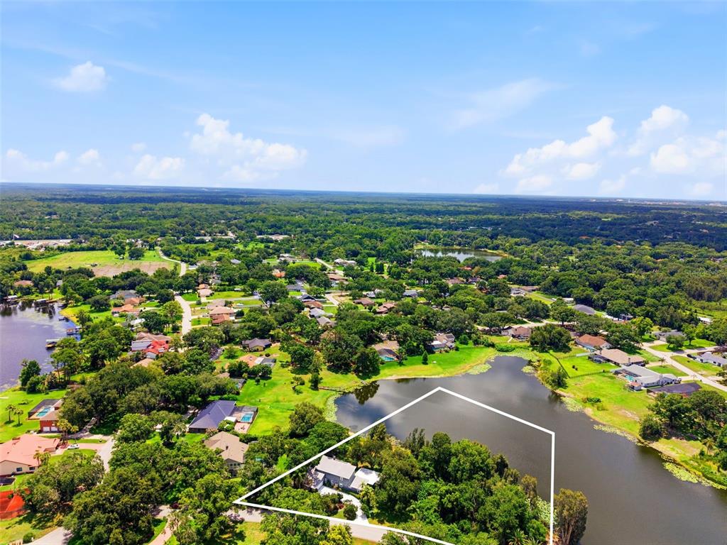 An aerial view shows a house on a wooded lot bordering a lake — 708 WARREN ROAD, LUTZ, FL