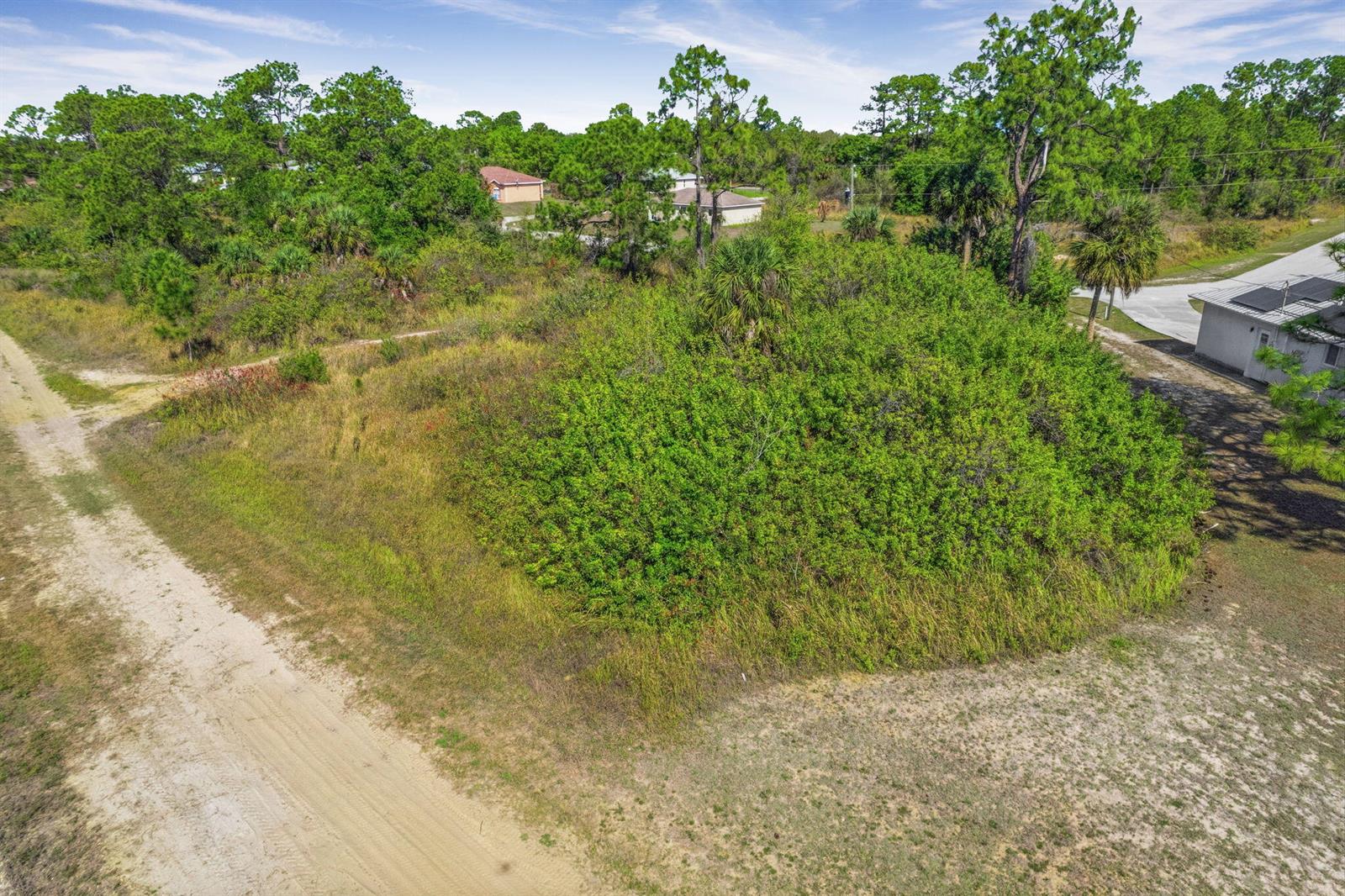 An aerial view shows a vacant, overgrown lot bordered by a dirt road and trees — 755 Longbow Lane, Lehigh Acres FL 33972, LEHIGH ACRES, FL