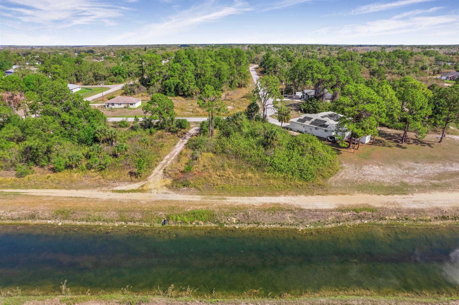 An aerial view shows a canal, a dirt road, and a house with solar panels — 755 Longbow Lane, Lehigh Acres FL 33972, LEHIGH ACRES, FL