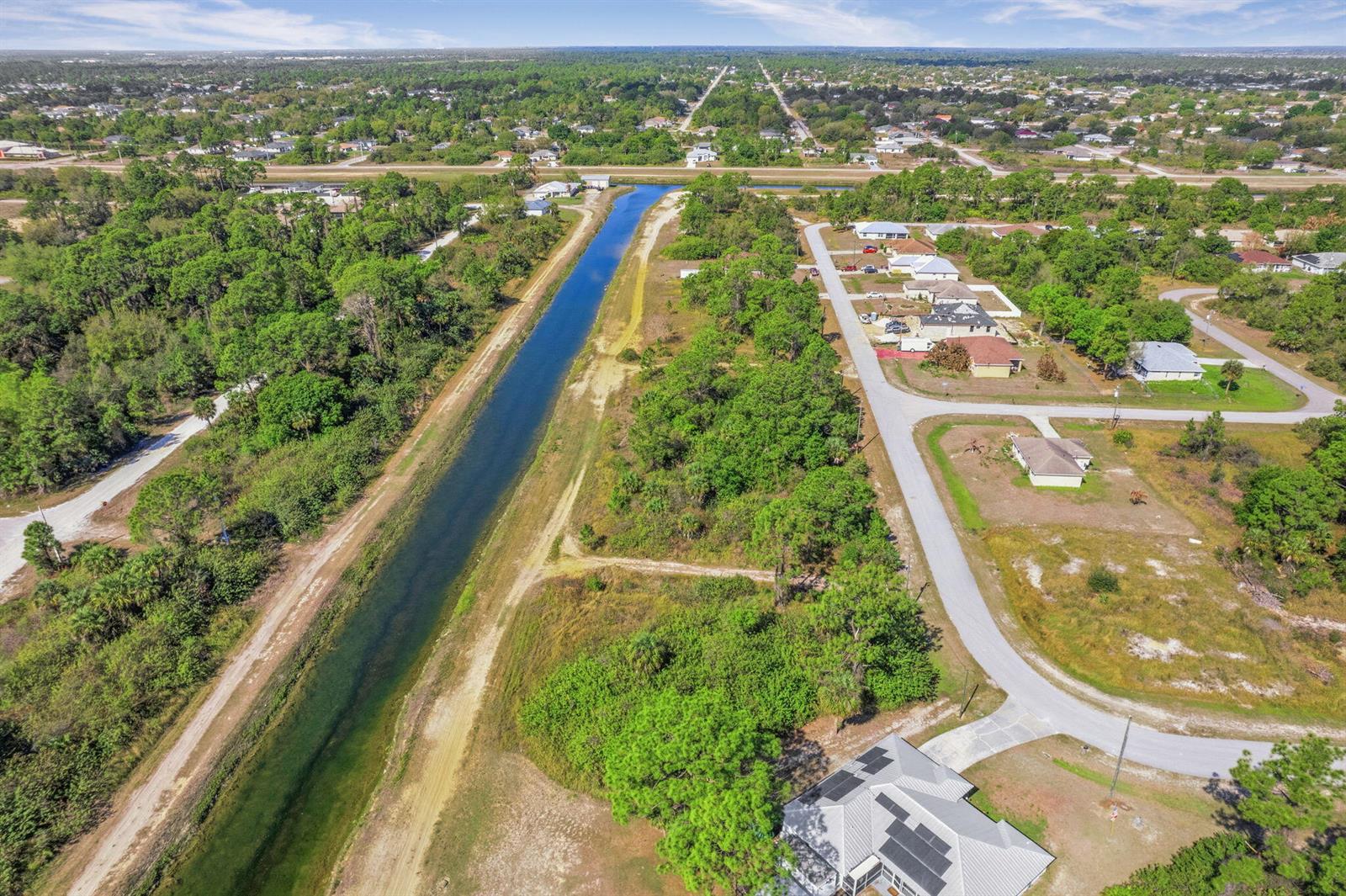 An aerial view shows a canal running alongside a residential street with scattered houses — 755 Longbow Lane, Lehigh Acres FL 33972, LEHIGH ACRES, FL