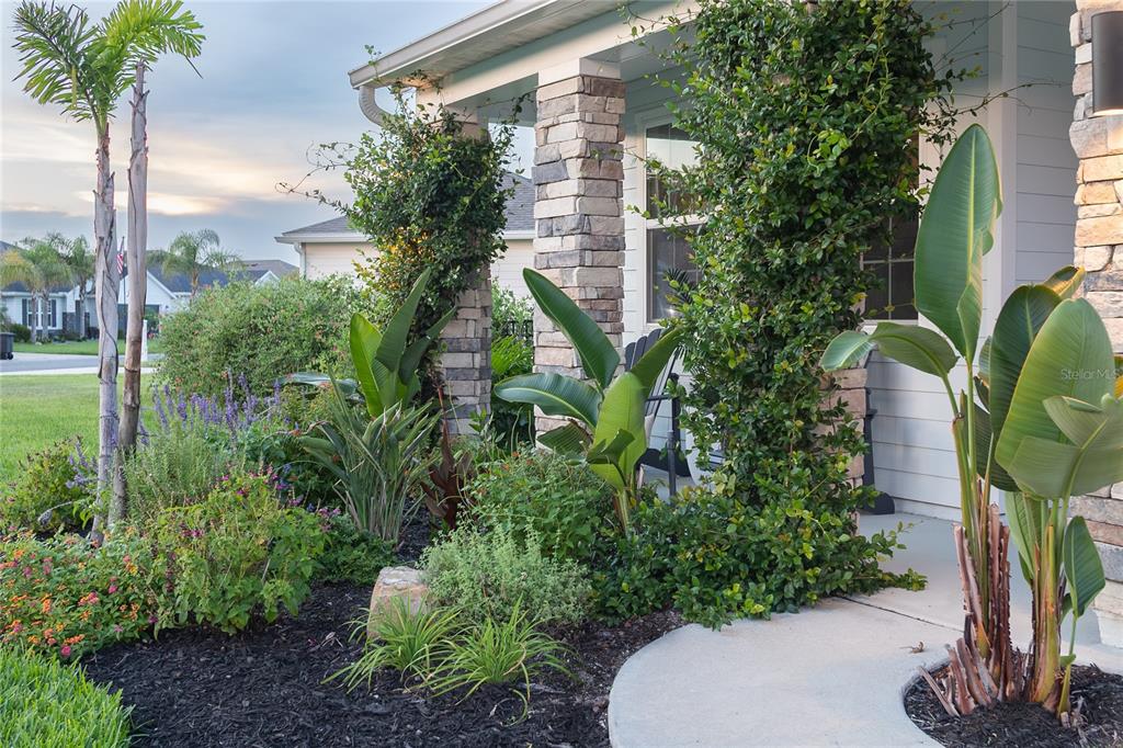 A stone-columned front porch features lush landscaping with tropical plants and climbing vines — 61 LAS CASITAS BOULEVARD, PALM COAST, FL