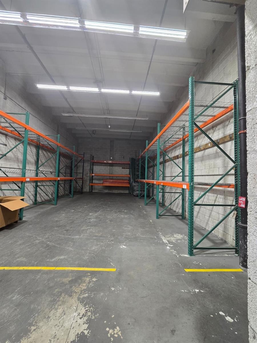 An industrial warehouse space features concrete walls, overhead lighting, and metal storage racking systems — 7953 NW 64th St, Medley FL 33166, MEDLEY, FL