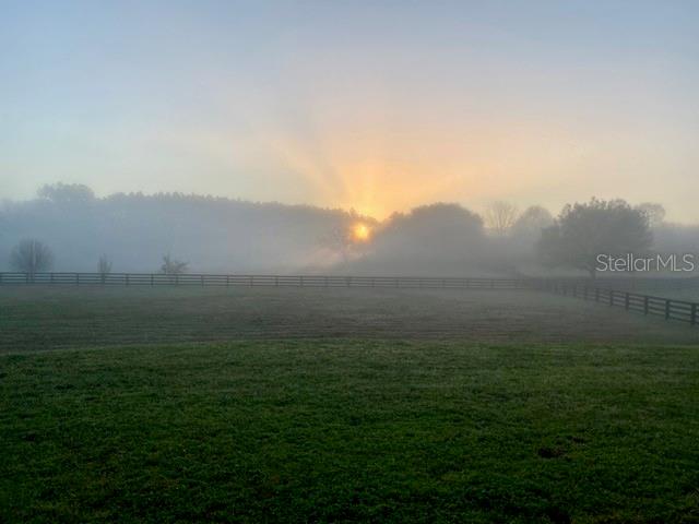 A sunrise shines over a foggy, fenced-in grassy pasture with trees in the background — 15681 NW 48TH PLACE, ALACHUA, FL