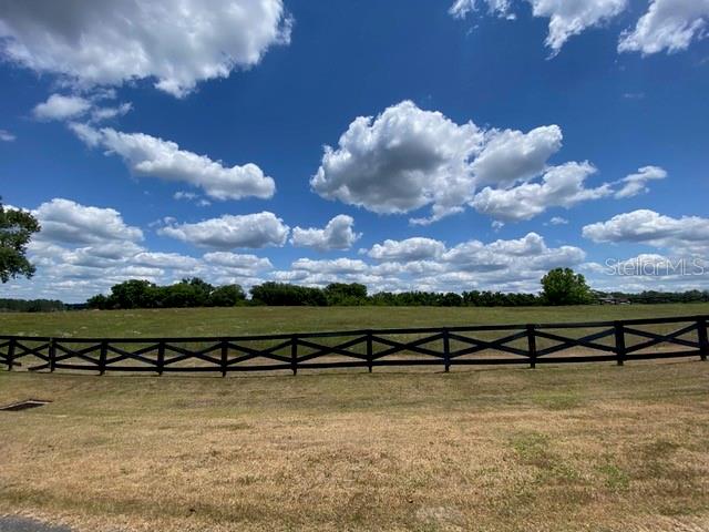 A black wooden fence borders a large, grassy field under a bright, cloudy blue sky — 15681 NW 48TH PLACE, ALACHUA, FL