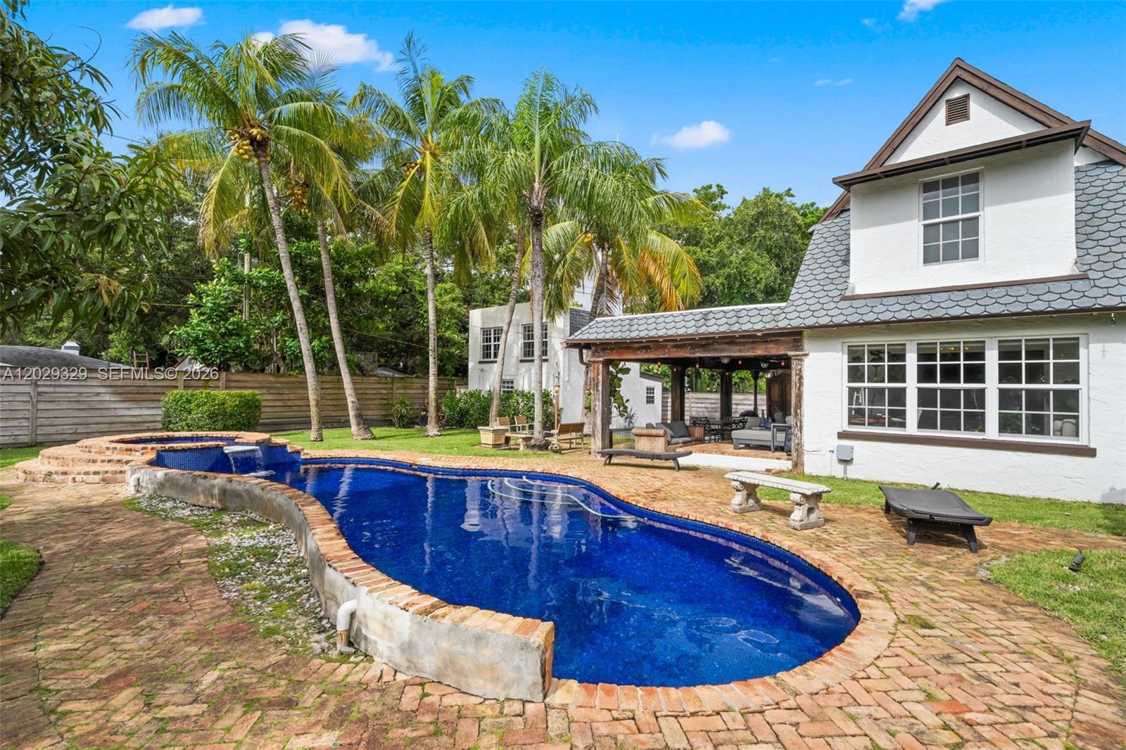 A backyard features a curved swimming pool with a brick deck and a white house — 646 NE 81st St, Miami FL 33138, MIAMI, FL