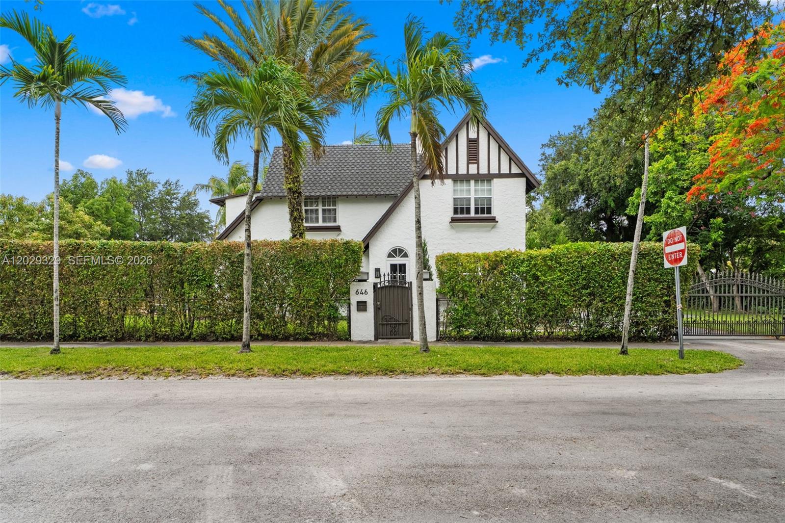 A two-story white house with a dark roof and timber accents sits behind a hedge — 646 NE 81st St, Miami FL 33138, MIAMI, FL