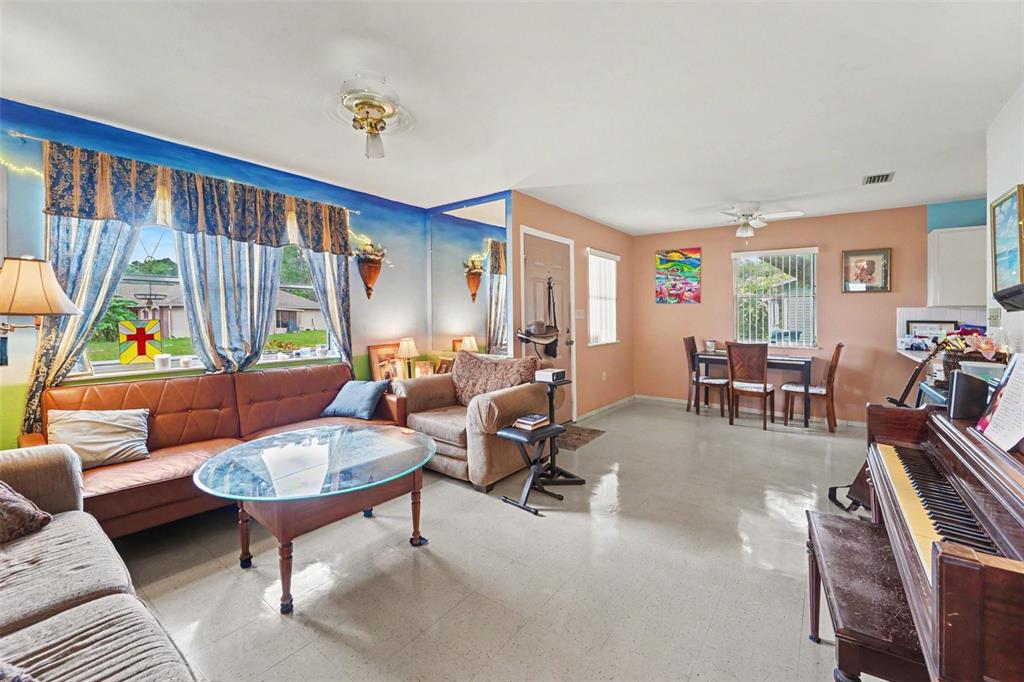 A living room with a piano, a brown sofa, a glass coffee table, and dining area — 12155 BAGDAD STREET, SPRING HILL, FL