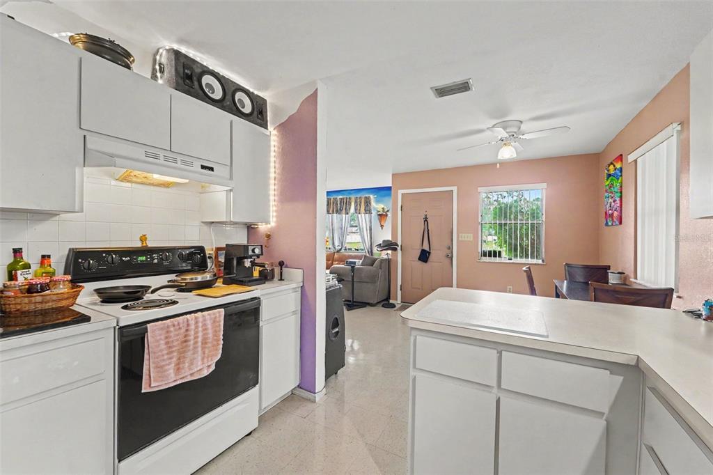 A kitchen with white cabinets and a black stove opens into a dining area — 12155 BAGDAD STREET, SPRING HILL, FL