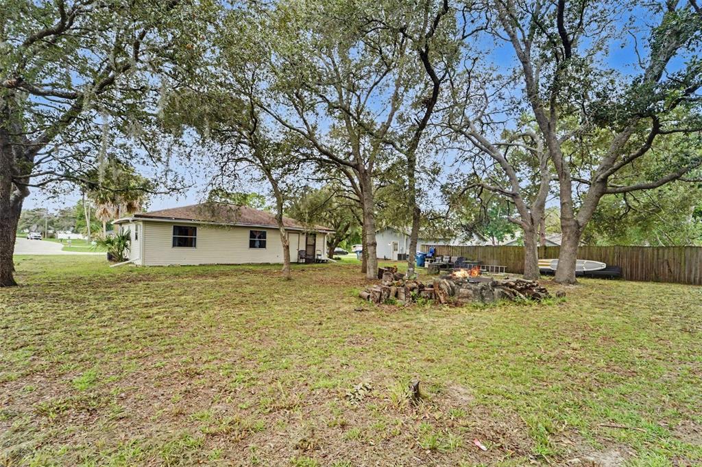 A backyard with a fire pit, mature trees, and a beige house with a wooden fence — 12155 BAGDAD STREET, SPRING HILL, FL