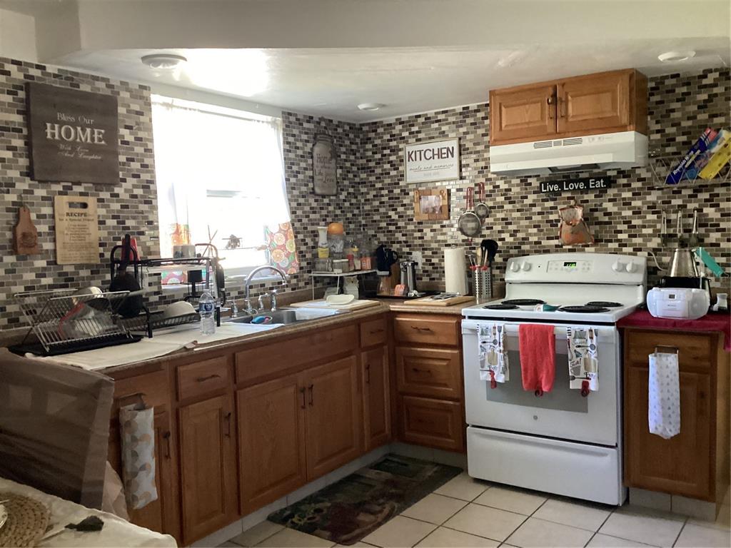A kitchen features wood cabinets, a white stove, and a tiled backsplash with decorative wall signs — 10029 BRANDYWINE AVENUE, PORT RICHEY, FL