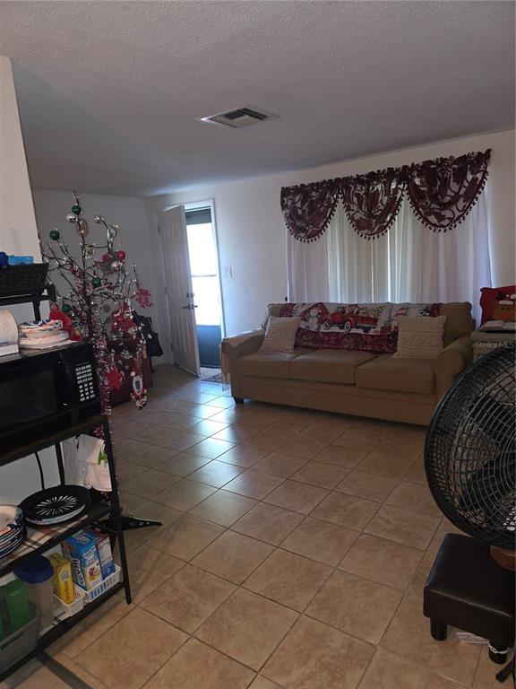 A living room with tile flooring, a tan sofa, a Christmas tree, and an entryway door — 10029 BRANDYWINE AVENUE, PORT RICHEY, FL