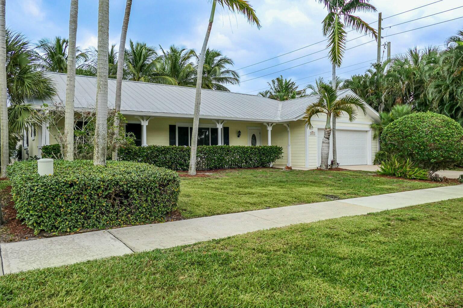 A single-story yellow house with a metal roof, palm trees, and a manicured lawn — 18014 Perigon Way, Jupiter FL 33458, JUPITER, FL