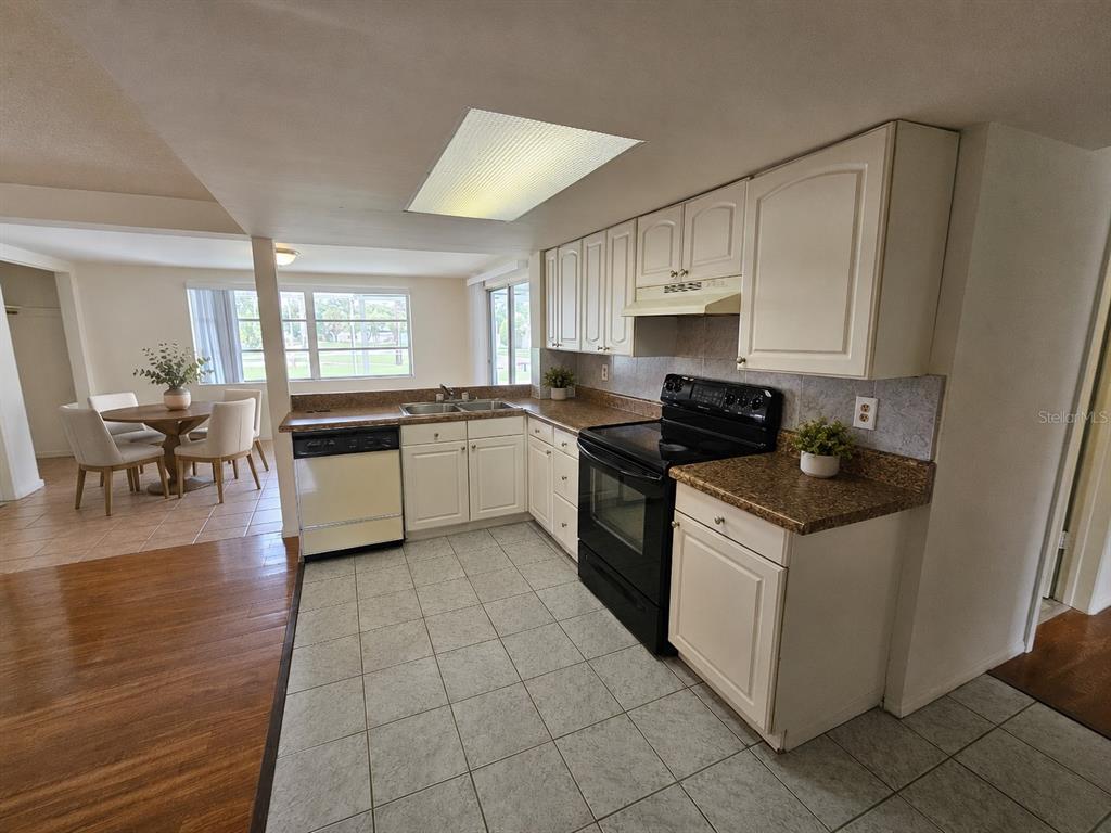 A kitchen with white cabinets, granite countertops, and black appliances opens to a dining area — 6945 TWILITE DRIVE, PORT RICHEY, FL