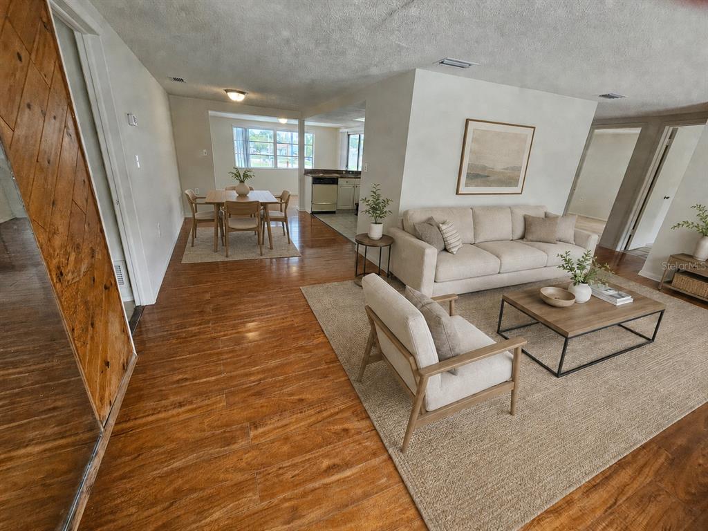 An open-concept living and dining area features wood-look flooring, neutral furniture, and a kitchen beyond — 6945 TWILITE DRIVE, PORT RICHEY, FL