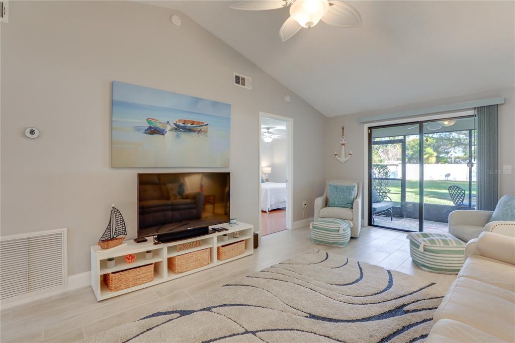 A living room features a television on a white console, a patterned rug, and sliding doors — 6010 36TH AVENUE CIRCLE W, BRADENTON, FL